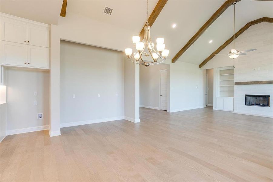 Unfurnished living room featuring beamed ceiling, light wood-type flooring, built in shelves, and a tiled fireplace