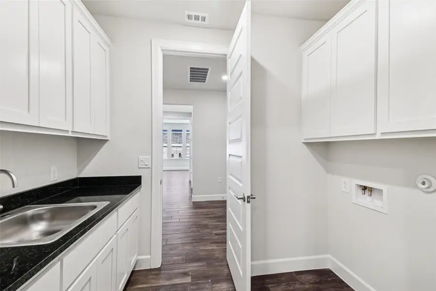 Washroom with cabinet space, hookup for a washing machine, and dark wood-style flooring