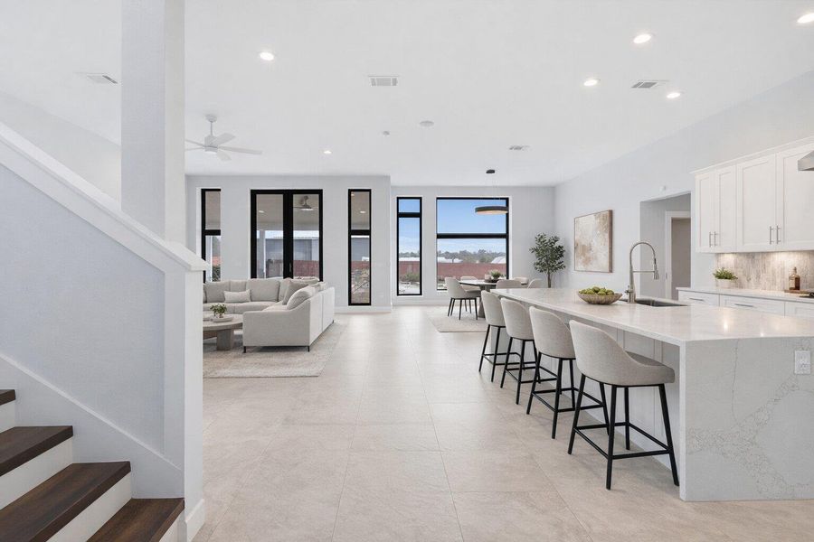 Kitchen featuring white cabinets, light stone countertops, decorative backsplash, a kitchen bar, and a spacious island