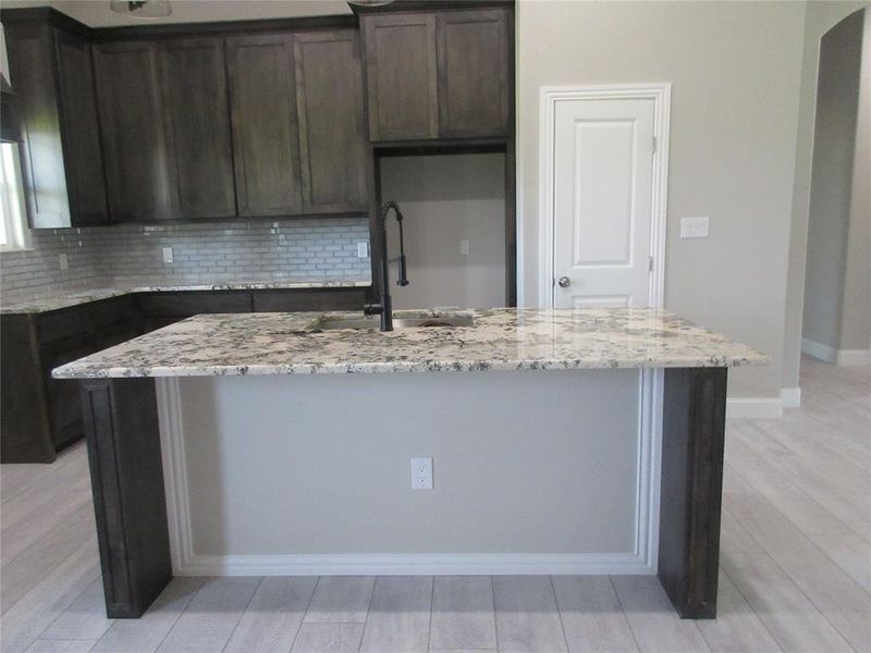 Kitchen featuring sink, dark brown cabinets, backsplash, light stone countertops, and a center island