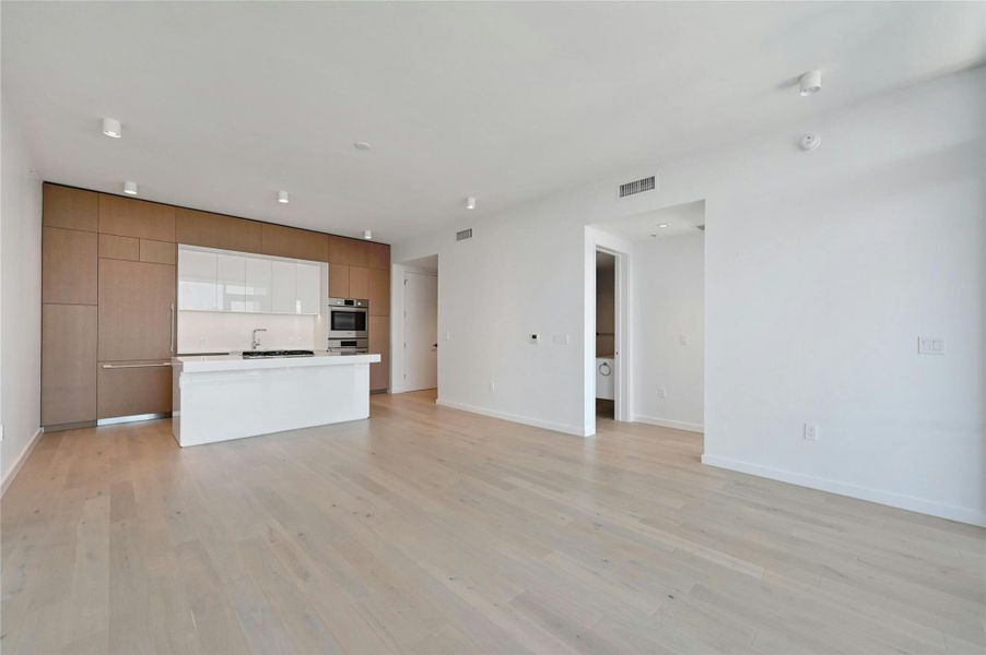 Sophisticated open-concept kitchen featuring sleek Bosch appliances, integrated wood-paneled cabinetry, and a glossy white island ideal for casual dining or entertaining—all seamlessly connected to the main living space with clean, modern lines.