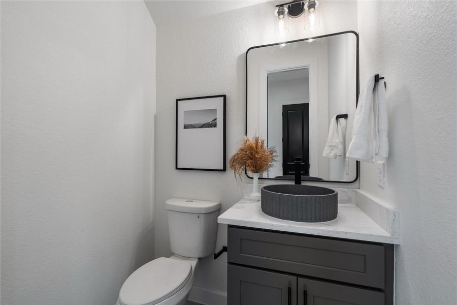 Powder bath with quartz vanity, textured vessel sink, and matte black accents. Powder bath with quartz vanity, textured vessel sink, and matte black accents.
