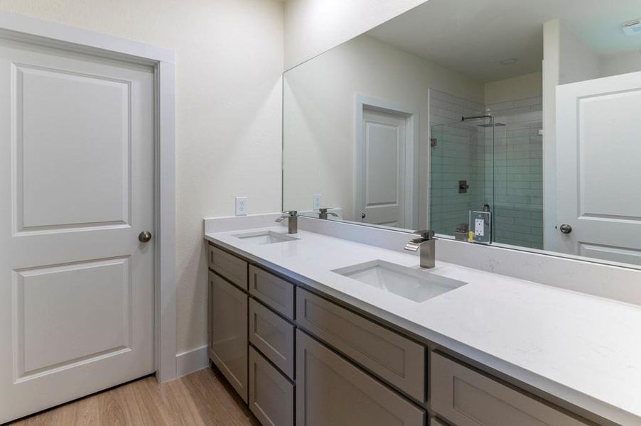 Full bathroom with double vanity, a shower stall, and light wood-type flooring