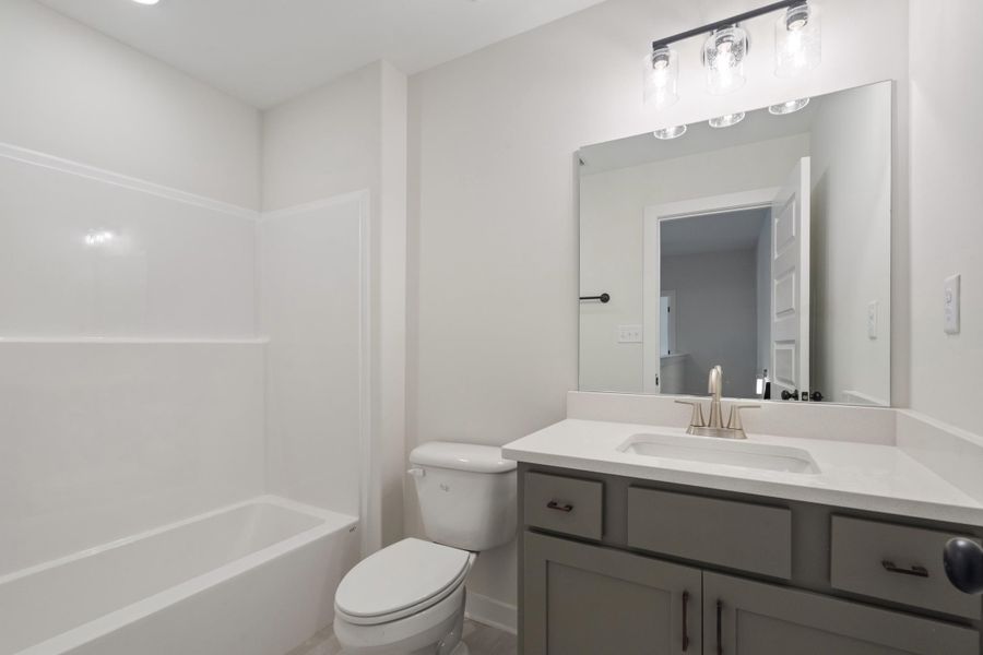 White bathtub and shower surround, light gray vanity with a white countertop, rectangular sink with a brushed nickel faucet, and a large wall-mounted mirror