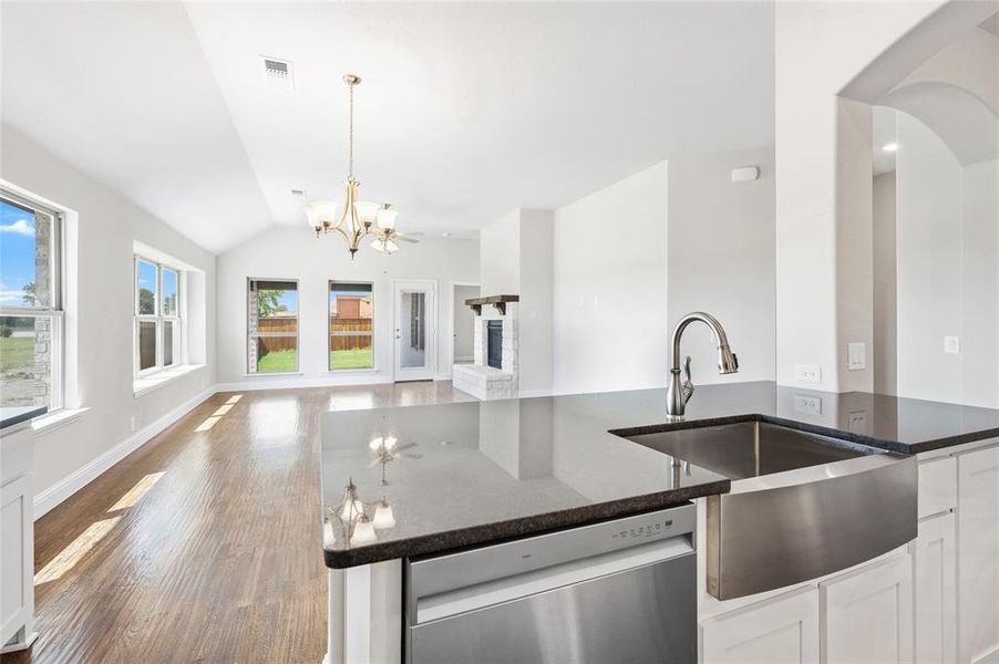 Kitchen with dark stone countertops, white cabinets, a chandelier, vaulted ceiling, and stainless steel dishwasher Kitchen with dark stone countertops, white cabinets, a chandelier, vaulted ceiling, and stainless steel dishwasher