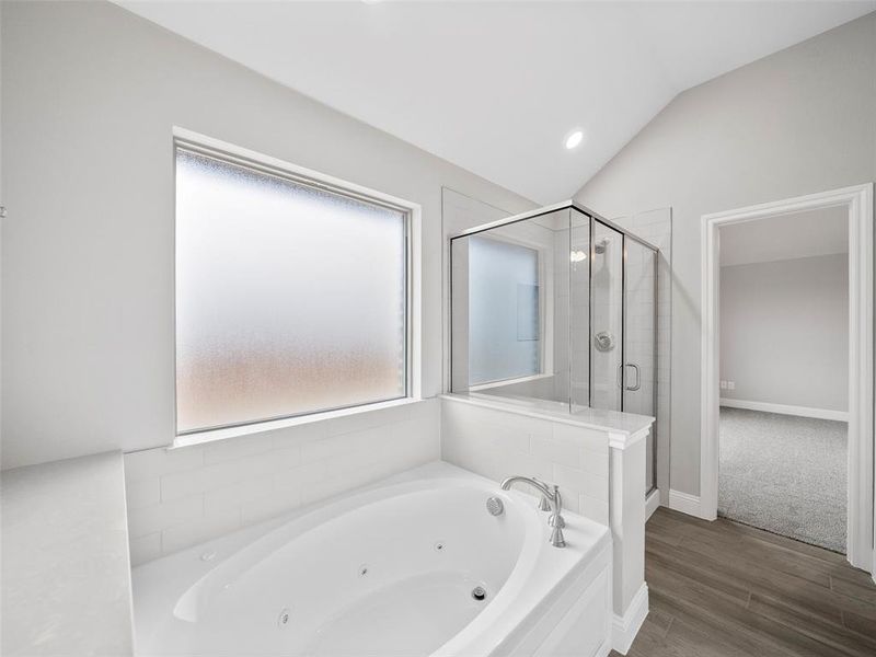 Full bathroom with wood finished floors, a whirlpool tub, lofted ceiling, a stall shower, and baseboards