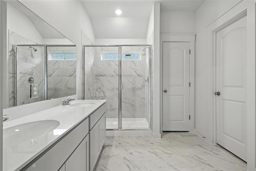 Full bath with a marble finish shower, marble look tile flooring, and double vanity