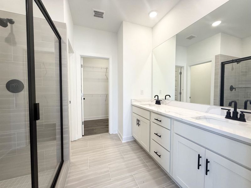 Bathroom with a stall shower, double vanity, and a walk in closet