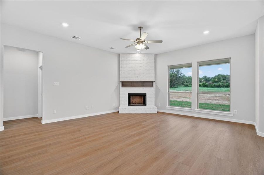 Living area featuring a corner white-painted brick fireplace with a wood mantel, wood-finish flooring, recessed lighting, and a ceiling fan