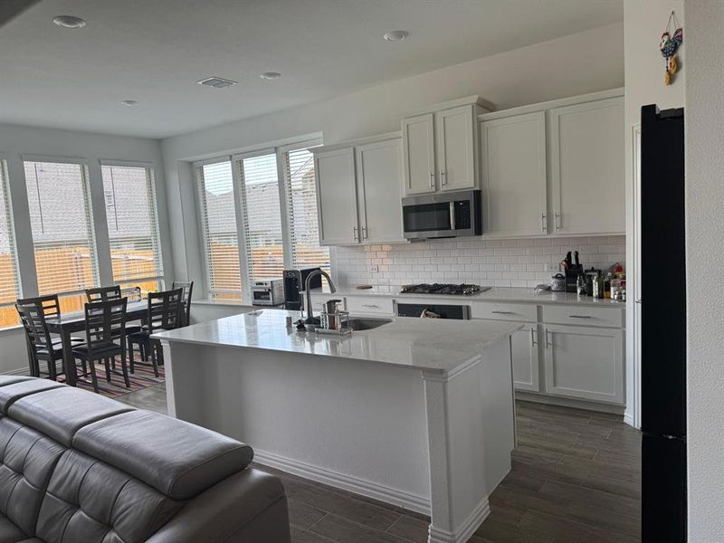 Bright kitchen featuring white shaker cabinetry, stainless steel appliances, a white subway tile backsplash, and light-toned countertops Bright kitchen featuring white shaker cabinetry, stainless steel appliances, a white subway tile backsplash, and light-toned countertops