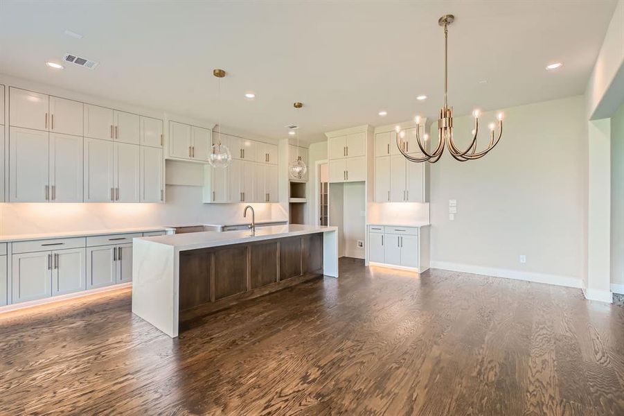 Kitchen featuring dark wood-style flooring, a chandelier, an island with sink, recessed lighting, and white cabinets Kitchen featuring dark wood-style flooring, a chandelier, an island with sink, recessed lighting, and white cabinets