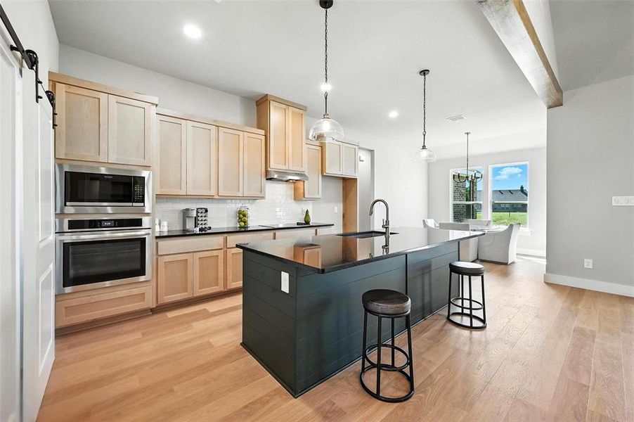 Kitchen featuring light wood finish cabinets, stainless steel appliances, a breakfast bar, pendant lighting, and a barn door