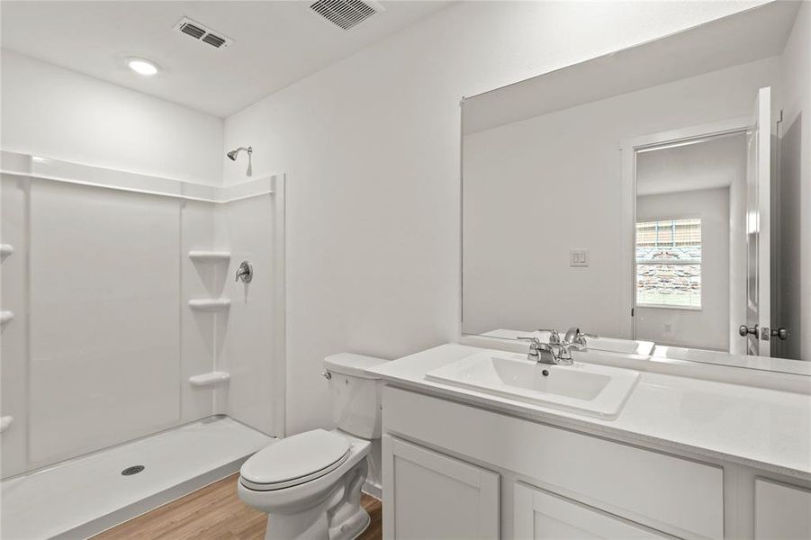 Full bathroom featuring a single-basin vanity with a white countertop, a large wall-mounted mirror, a commode, a shower enclosure, and wood-finish flooring
