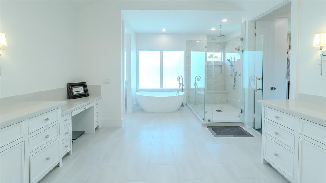 This spacious bathroom features a modern design with a freestanding bathtub, a large glass-enclosed shower, and ample storage with white cabinetry. The room is bright and airy, enhanced by natural light from the large window.