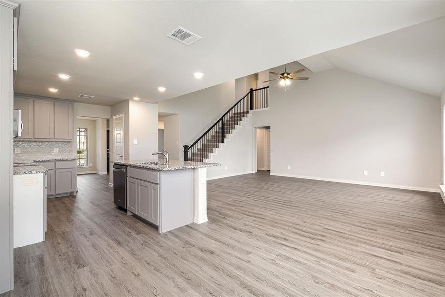 Kitchen featuring light stone countertops, light wood-type flooring, gray cabinetry, vaulted ceiling, and a kitchen island with sink