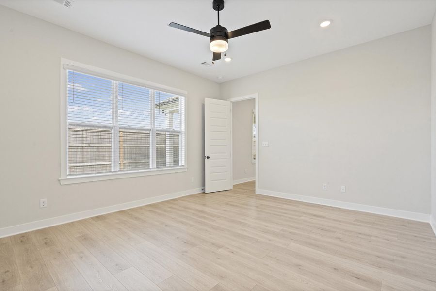 Spacious room featuring wood-finish flooring, a large window with blinds, and white trim Spacious room featuring wood-finish flooring, a large window with blinds, and white trim