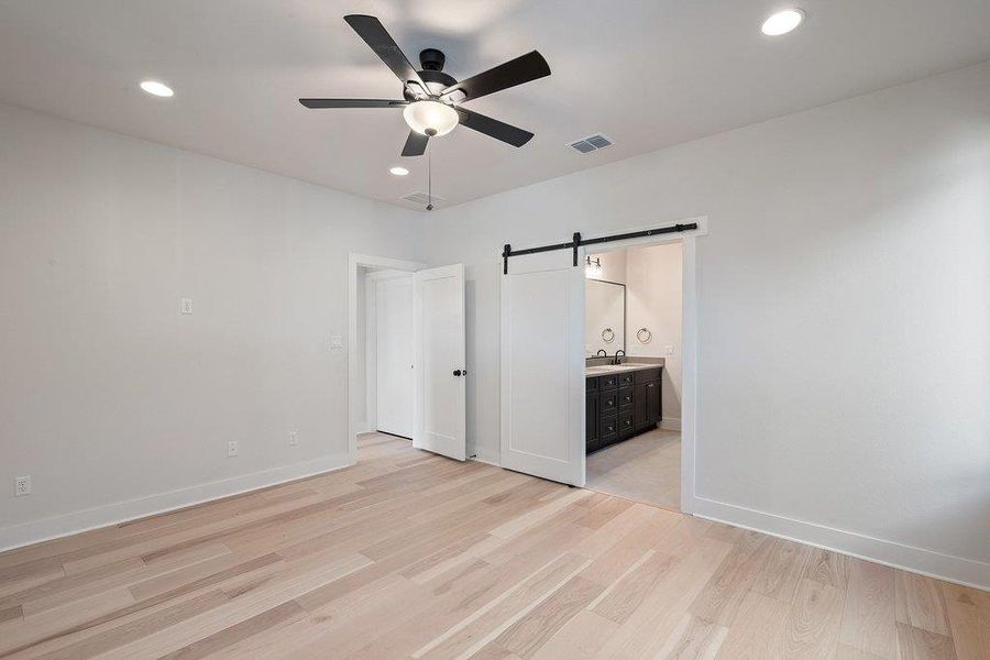 Unfurnished bedroom with a barn door, recessed lighting, light wood finished floors, ceiling fan, and ensuite bathroom