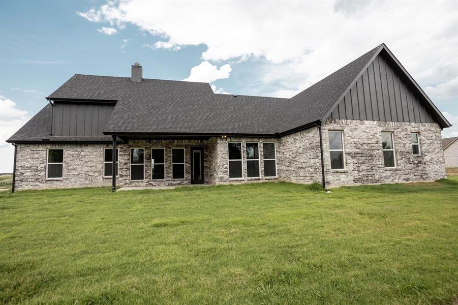 Back of house with board and batten siding, a patio area, a lawn, and brick siding Back of house with board and batten siding, a patio area, a lawn, and brick siding