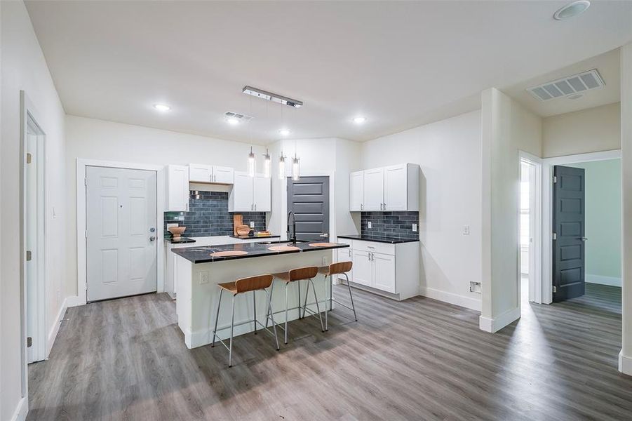 Kitchen with a kitchen bar, white cabinets, hardwood / wood-style flooring, and tasteful backsplash