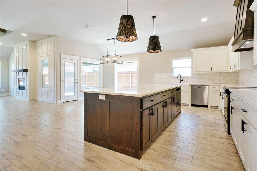 Kitchen with decorative backsplash, white cabinetry, hanging light fixtures, and appliances with stainless steel finishes