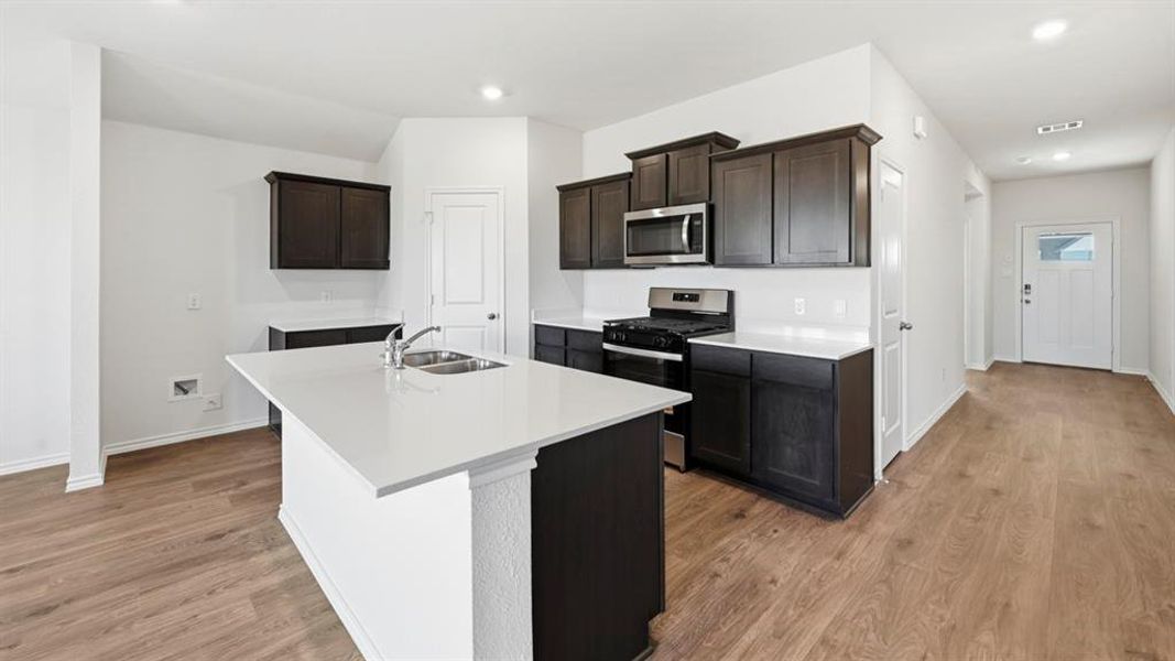 Kitchen featuring appliances with stainless steel finishes, a kitchen island with sink, dark brown cabinets, light wood-style floors, and recessed lighting