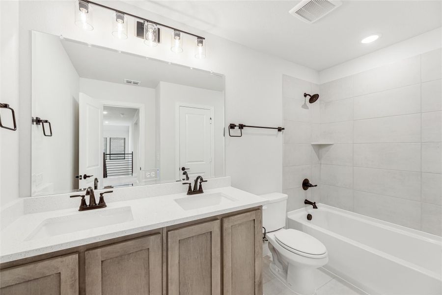 Bathroom with double vanity, white countertop, tub-shower combo, and large mirror with pendant lights