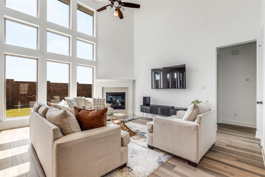 Living room featuring a towering ceiling, a premium fireplace, light wood finished floors, and a ceiling fan