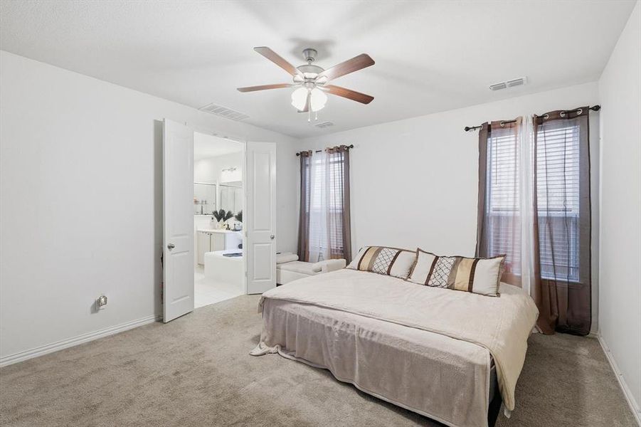 Bedroom featuring ceiling fan, light carpet, and ensuite bath