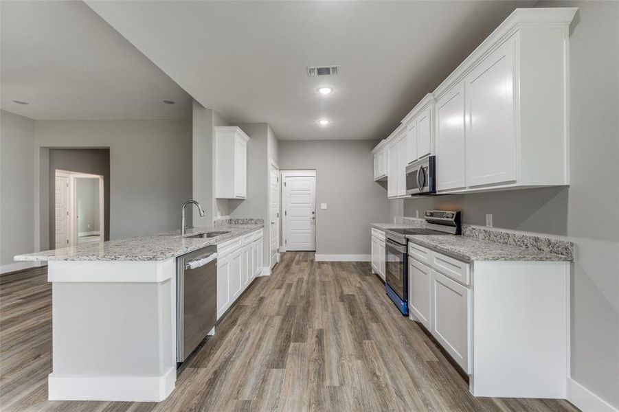 Kitchen with stainless steel appliances, light stone countertops, a peninsula, white cabinetry, and recessed lighting