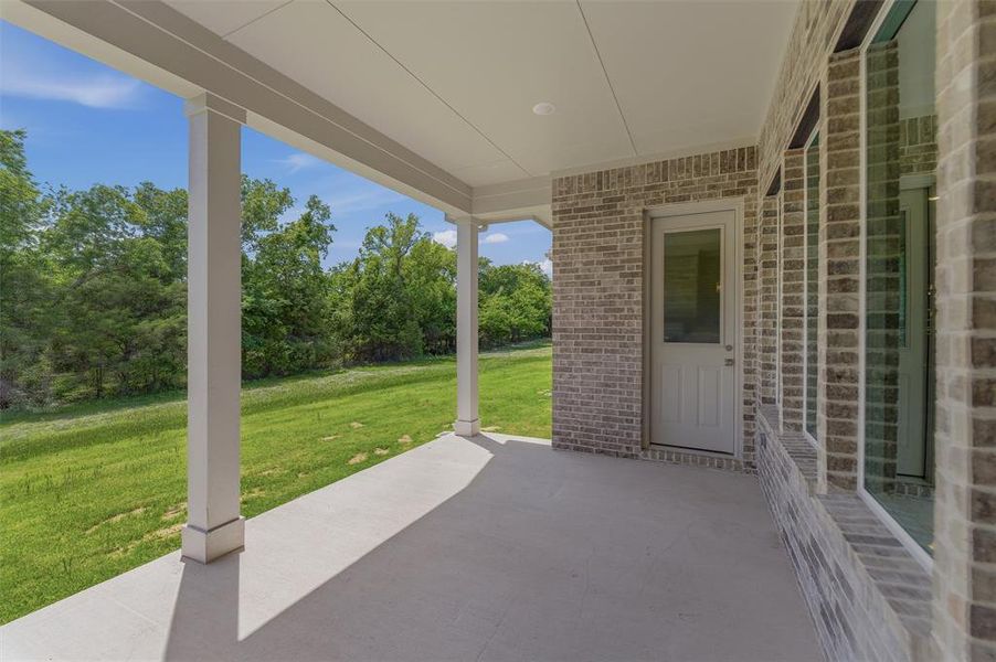 Covered concrete patio featuring white support columns and a light brick exterior