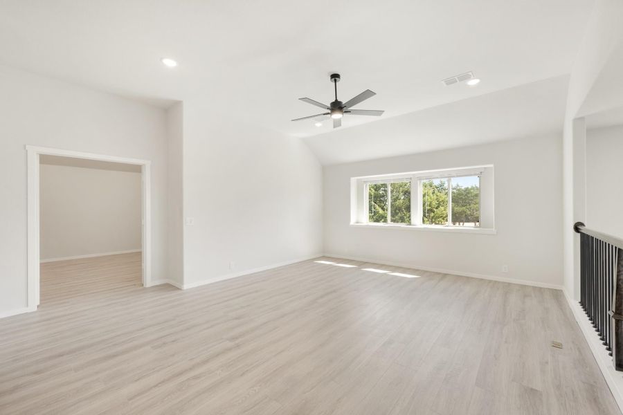 Empty room with vaulted ceiling, ceiling fan, light wood floors, and a wide window