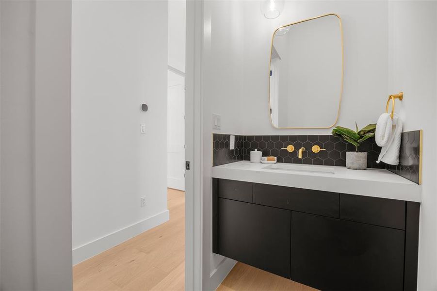Elegant powder room featuring a floating vanity with a vessel sink and chic gold fixtures.