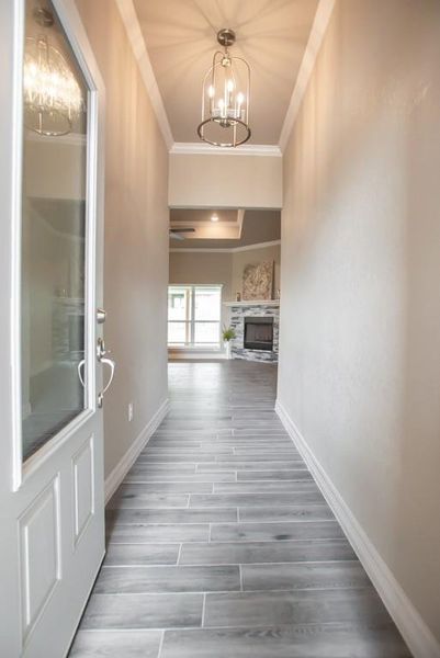 Hallway with a chandelier, crown molding, and wood finished floors Hallway with a chandelier, crown molding, and wood finished floors
