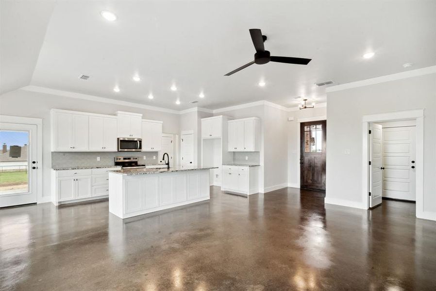 Kitchen with appliances with stainless steel finishes, tasteful backsplash, a center island with sink, concrete flooring, and ceiling fan