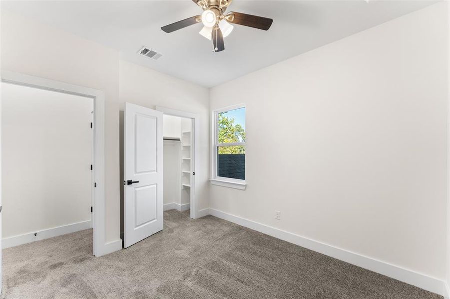 Unfurnished bedroom with a spacious closet, light colored carpet, and ceiling fan Unfurnished bedroom with a spacious closet, light colored carpet, and ceiling fan