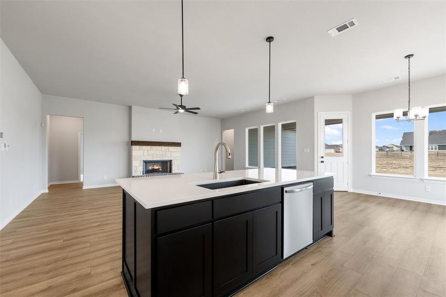 Kitchen with dark cabinetry, a stone fireplace, open floor plan, a chandelier, and an island with sink Kitchen with dark cabinetry, a stone fireplace, open floor plan, a chandelier, and an island with sink