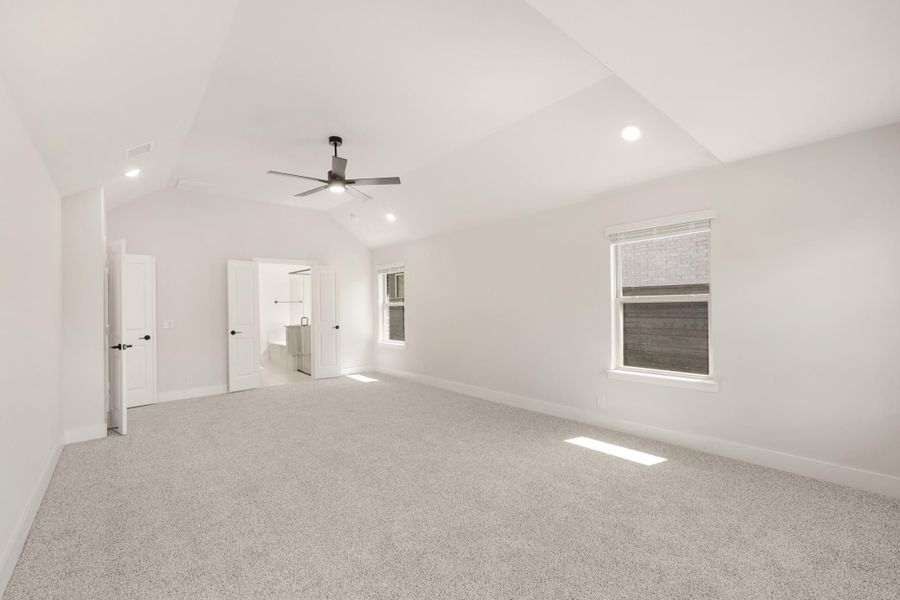 Spacious bedroom with vaulted ceiling, ceiling fan, carpet flooring, and ensuite bathroom doorway