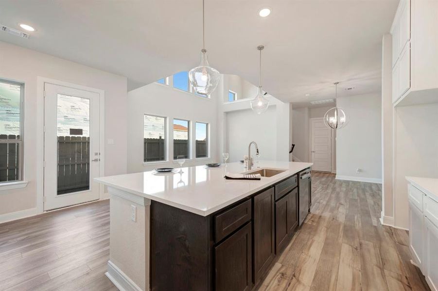 Two tone kitchen with light wood finished floors, a kitchen island with sink, light stone counters, stainless steel dishwasher, and two tone cabinetry
