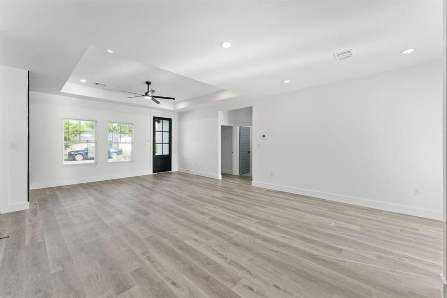 Unfurnished living room featuring light hardwood / wood-style flooring, a tray ceiling, and ceiling fan