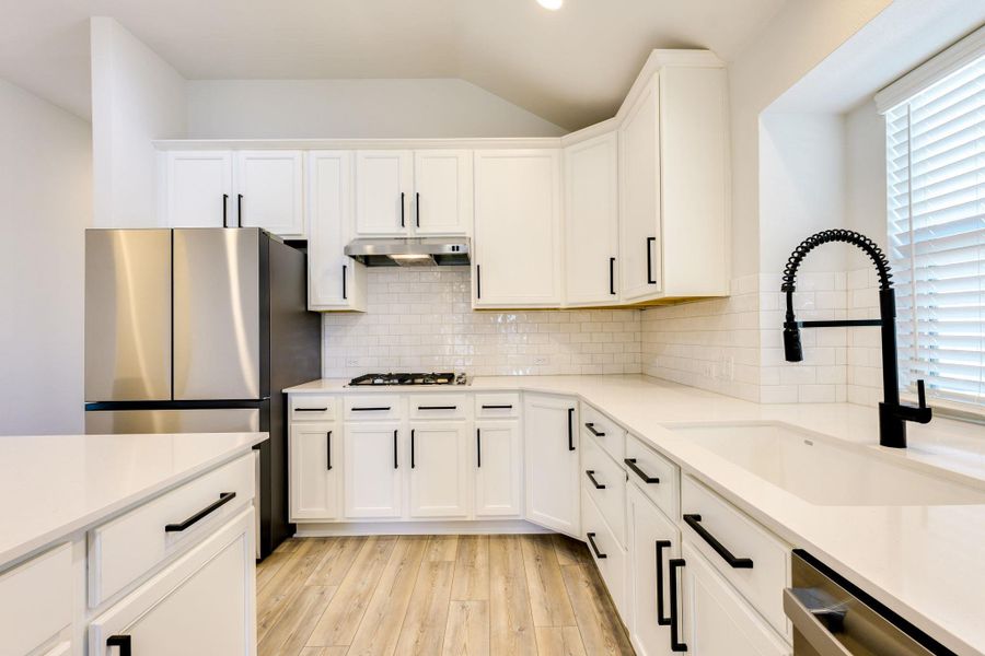 Kitchen featuring appliances with stainless steel finishes, plenty of natural light, white cabinetry, vaulted ceiling, and recessed lighting