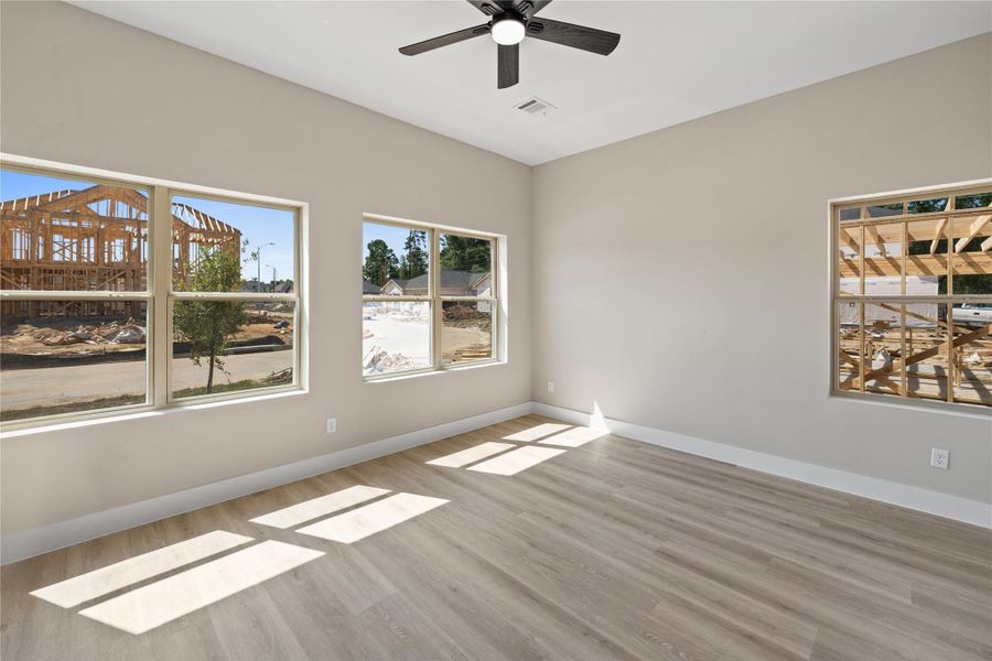Bright room with large windows, light wood flooring, and a ceiling fan. Views of ongoing construction outside suggest a developing neighborhood. Bright room with large windows, light wood flooring, and a ceiling fan. Views of ongoing construction outside suggest a developing neighborhood.