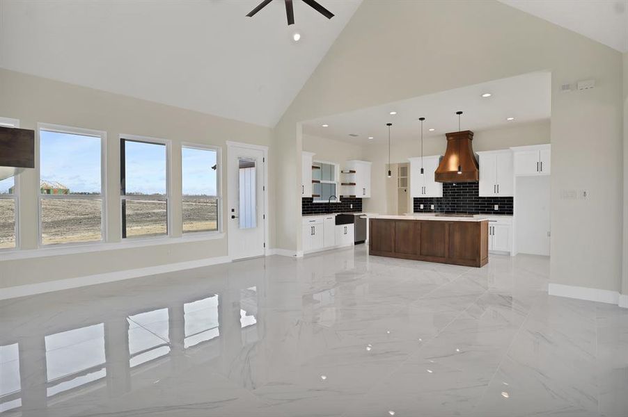 Kitchen featuring high vaulted ceiling, decorative light fixtures, backsplash, custom exhaust hood, and a center island