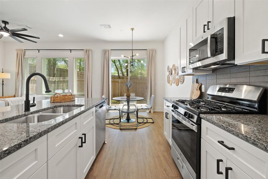 Kitchen featuring appliances with stainless steel finishes, light wood-style flooring, white cabinets, decorative backsplash, and dark stone counters Kitchen featuring appliances with stainless steel finishes, light wood-style flooring, white cabinets, decorative backsplash, and dark stone counters
