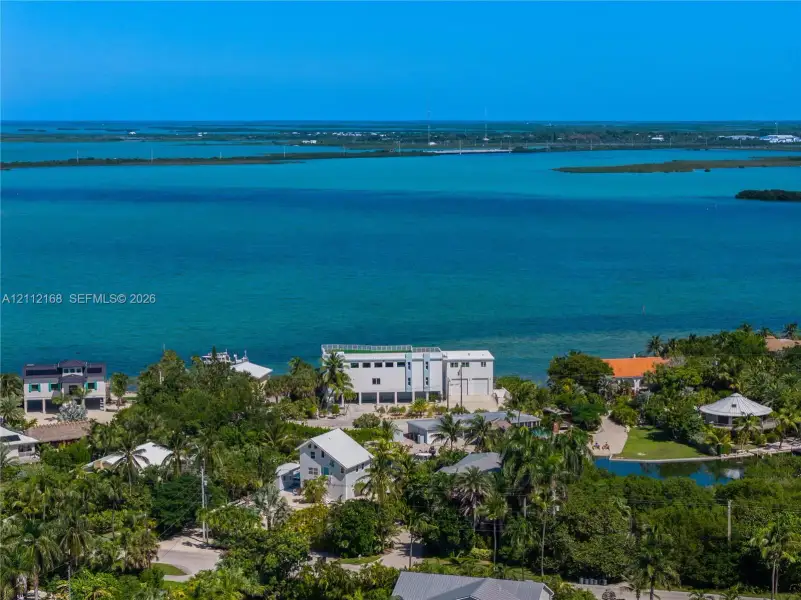 Waterfront property featuring direct coastal access, multi-level structural design, white exterior cladding, and expansive surrounding tropical vegetation Waterfront property featuring direct coastal access, multi-level structural design, white exterior cladding, and expansive surrounding tropical vegetation