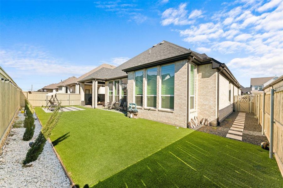 The property features a spacious backyard with artificial turf, a rock border with planted shrubs, and a paved patio area