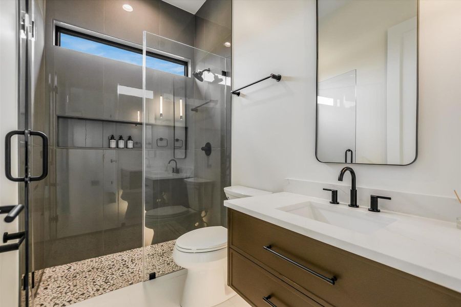 Modern bathroom featuring a glass-enclosed shower with contrasting tile, a rectangular vanity with a white countertop and integrated sink, matte black fixtures, and a frameless mirror