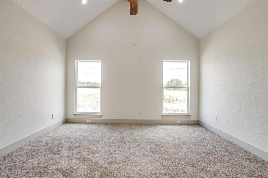 Carpeted empty room featuring a wealth of natural light, ceiling fan, and lofted ceiling with beams