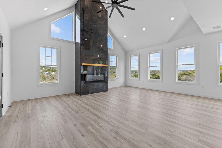 Unfurnished living room featuring a high ceiling, a large fireplace, ceiling fan, light wood-type flooring, and recessed lighting