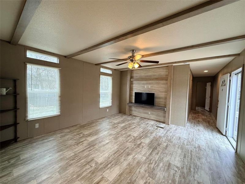 Unfurnished living room with a textured ceiling, a ceiling fan, beamed ceiling, wood walls, and light wood finished floors