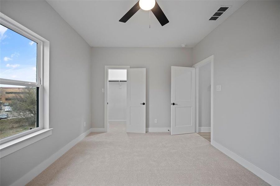 Unfurnished bedroom with a walk in closet, light colored carpet, visible vents, and baseboards